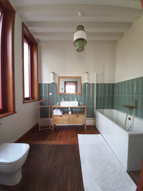 Modern bathroom at Villa Eliane in Étretat with wooden vanity, green tile wainscoting, white bathtub, and pendant lighting