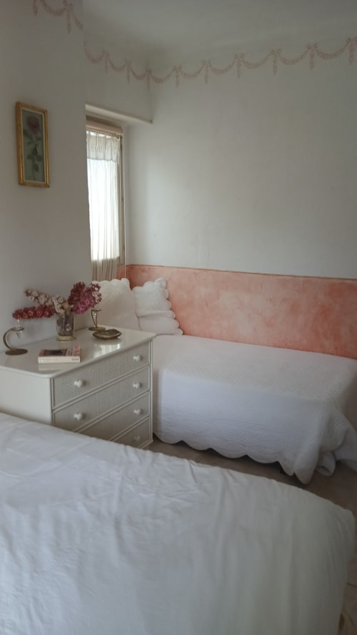 Chambre accueillante à La Ribeyrette avec tête de lit rose, literie blanche et table de nuit fleurie