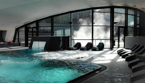 Piscine intérieure Zoppas Courchevel avec bain à remous, chaises longues et vue sur les montagnes par les baies vitrées