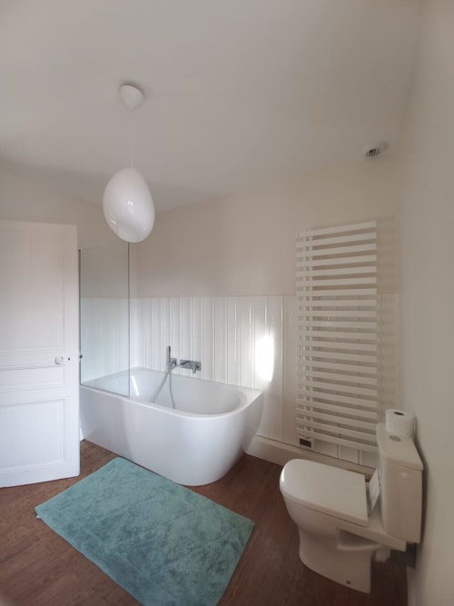 Modern bathroom at Villa Eliane with freestanding white bathtub, toilet, heated towel rack, and wooden flooring in Étretat