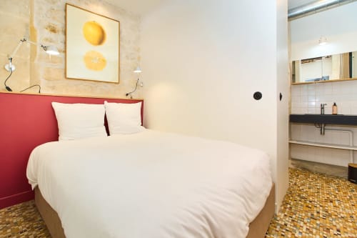 Chambre moderne au Boutik Boheme Paris avec tête de lit rouge, linge blanc, œuvre citron jaune et salle de bain attenante
