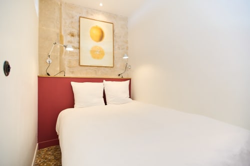 Chambre moderne à Boutik Boheme Paris avec tête de lit rouge, literie blanche et tableau de citrons au-dessus du lit au Loft Menilmontant