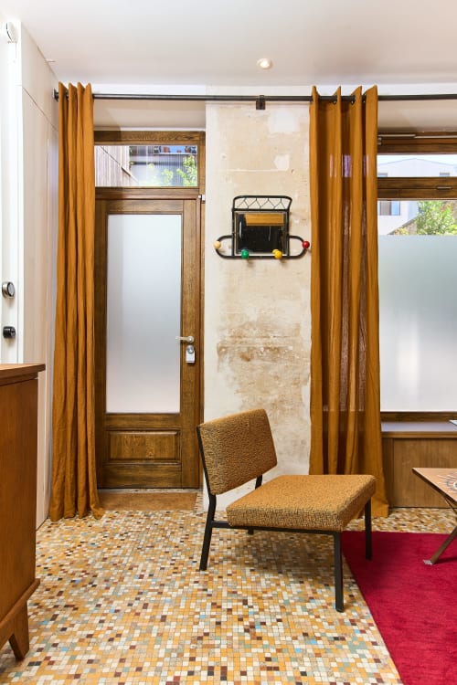 Entrée de l'appartement Boutik Boheme Paris avec portes en bois, rideaux dorés, carrelage mosaïque et chaise années 50