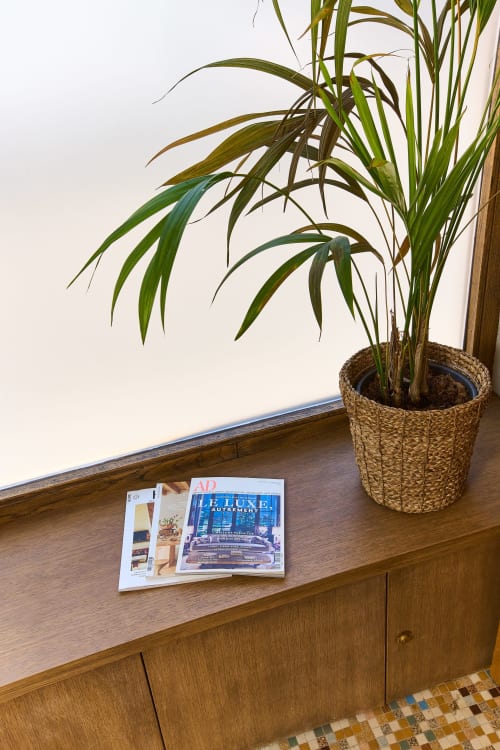 Commode en bois avec magazines dans un loft parisien, plante en pot dans un panier tressé contre un mur blanc