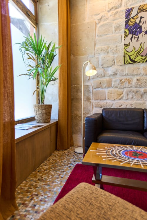 Salon chaleureux de Boutik Boheme Paris avec canapé en cuir noir, plante en pot près de la fenêtre, tapis géométrique et murs en brique