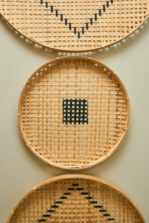 Trois paniers tressés en bambou aux motifs géométriques noirs exposés sur un mur blanc à la Boutik Boheme Paris