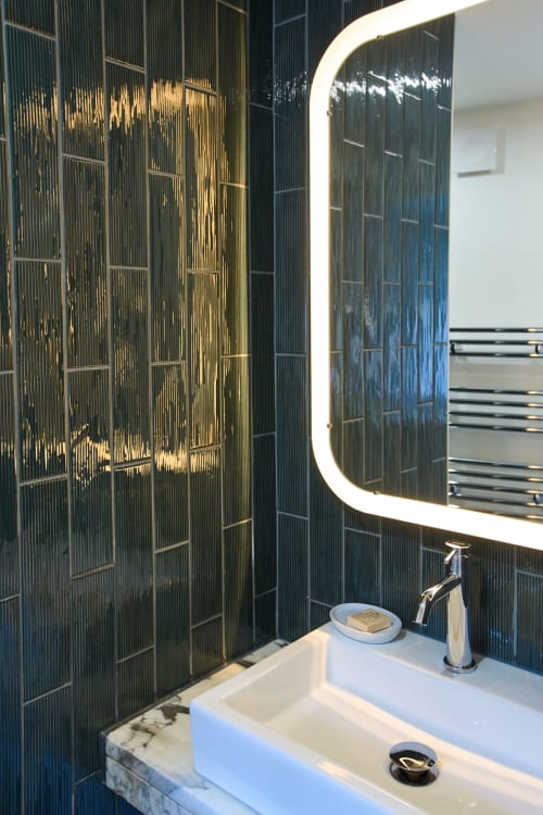 Salle de bain moderne au Boutik Boheme Paris avec carrelage noir, miroir rond éclairé, vasque en marbre et robinetterie chromée
