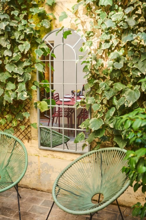 Vue du jardin à travers une fenêtre couverte de lierre à Boutik Boheme Paris avec chaises turquoise et coin repas