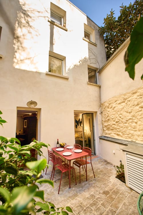 Patio cosy du Boutik Boheme à Paris avec table de salle à manger rouge, plantes en pot et murs en pierre crème