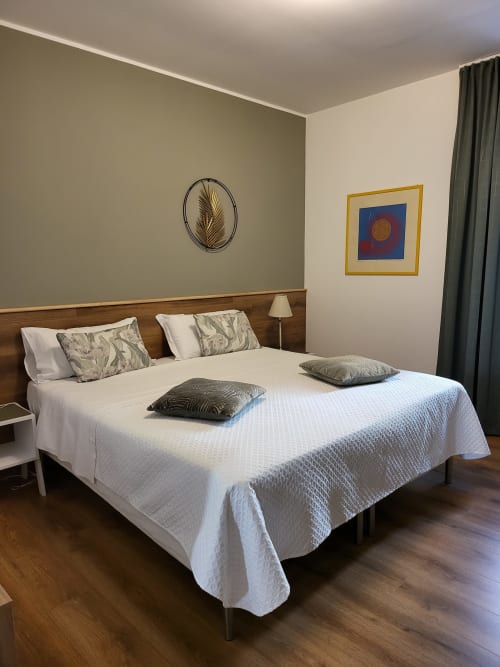 Camera deluxe presso Alloggi Tosca Airport Lodge con letto matrimoniale, testata in legno, parete d'accento verde oliva e opere d'arte incorniciate