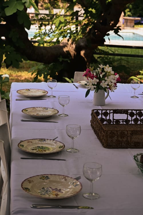 Table élégante dressée en plein air au Mas De La Digue avec assiettes à motifs floraux, verres à vin et fleurs fraîches avec vue panoramique
