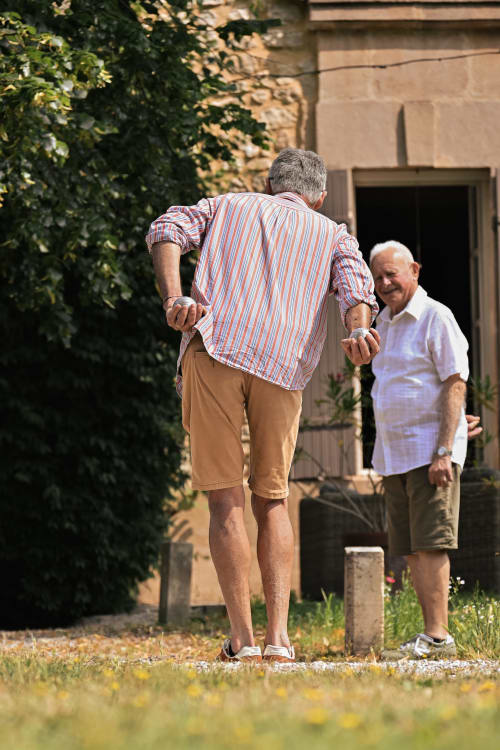 Deux hommes se saluent devant la maison d'hôtes Mas De La Digue à Châteaurenard, France, avec son bâtiment en pierre recouvert de lierre et sa cour.