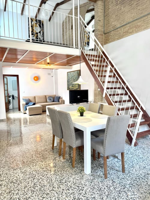 Apartamento loft moderno en Valencia con comedor diáfano, sala de estar, vigas vistas y escalera de caracol hacia el nivel de entresuelo