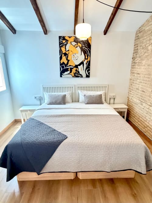 Dormitorio moderno en loft de Stay Gest Valencia con cama queen, arte amarillo-negro, vigas vistas y pared de ladrillo