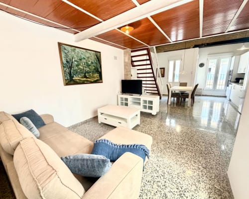 Sala de estar estilo loft moderno en Valencia con sofá beige, techo de madera, televisión y cocina al fondo