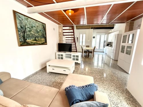 Salón moderno de apartamento en Valencia con techo de madera, sofá beige, muebles blancos y cocina integrada en Stay Gest