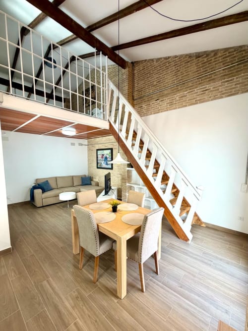 Área de comedor moderno en loft con mesa de madera, barandillas blancas, ladrillo visto y entresuelo en Stay Gest València