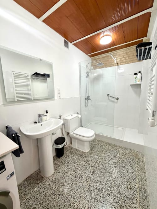 Baño moderno con ducha abierta, sanitarios blancos y techo de madera en Marqués Urban Loft Valencia