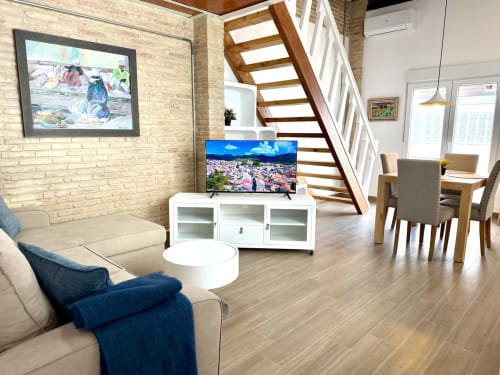 Moderno loft en Valencia con TV, sofá beige, escaleras de madera y vistas a la ciudad en Stay Gest