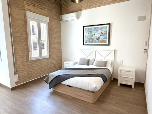 Moderno dormitorio en Marqués Urban Loft 2 Valencia con paredes de ladrillo, cama de madera, mesilla blanca y vistas a la ciudad