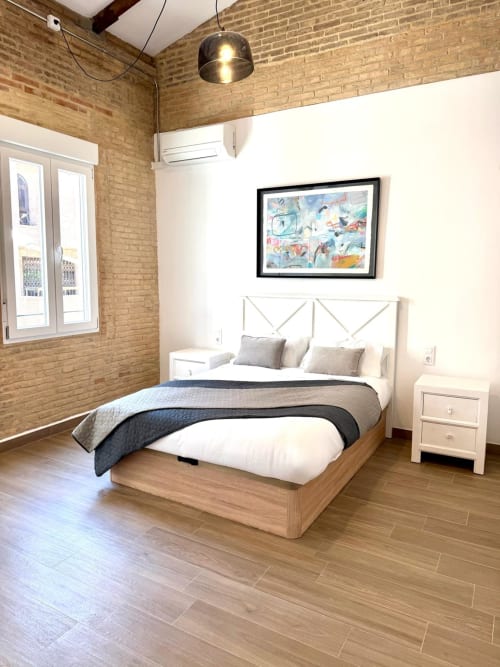 Habitación moderna en Marqués Urban Loft 2, Valencia: paredes de ladrillo, cama de madera, cabecero blanco y vistas a la ciudad desde el balcón