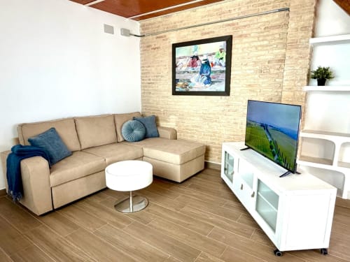 Salón moderno de apartamento en Valencia con sofá seccional beige, mueble TV blanco, pared de ladrillo y pantalla plana