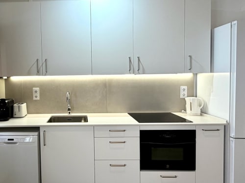 Cocina moderna blanca en Marqués Urban Loft, Valencia. Equipada con placa eléctrica, fregadero, horno negro e iluminación ambiental.