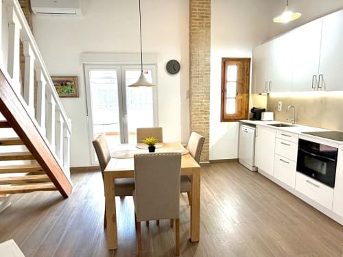 Cocina y comedor loft moderno en Valencia con muebles blancos, mesa de madera y detalles de ladrillo