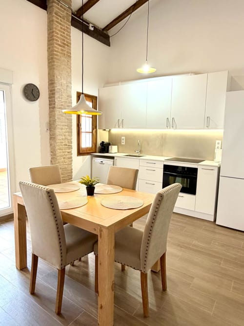 Cocina-comedor moderna en Marqués Urban Loft 2 Valencia con mesa de madera, sillas beige, gabinetes blancos y elementos expuestos