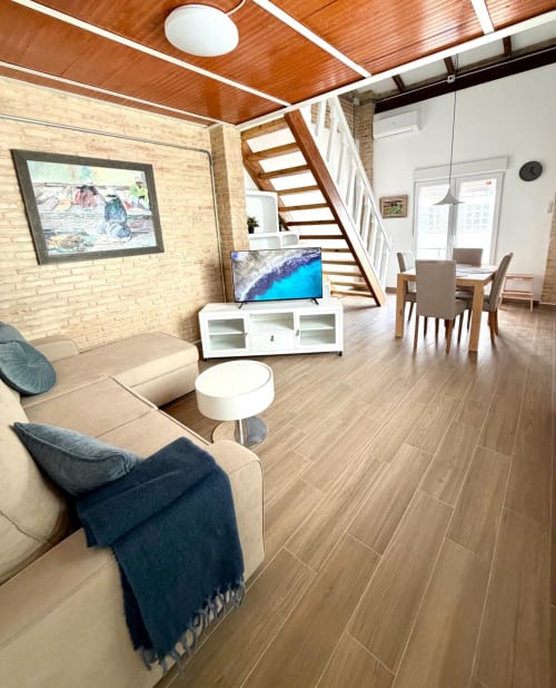 Moderno loft en Valencia con sofá beige, escaleras de madera, televisor, paredes de ladrillo y zona de comedor