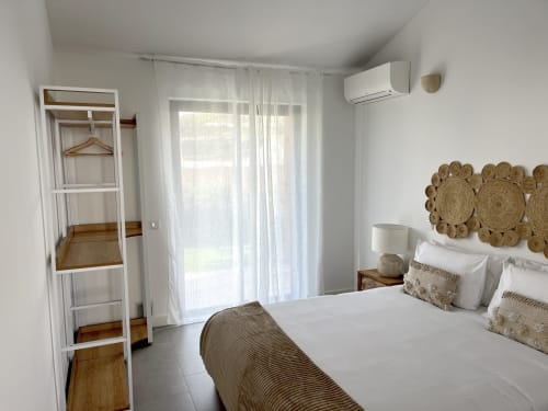 Bright bedroom at Casa Mareta villa in Bordeira with sea view, white bedding, woven wall décor, and modern air conditioning