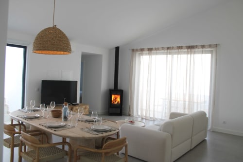 Modern villa dining and living room with wood stove, sea view terrace doors, and rustic pendant light at Casa Mareta,