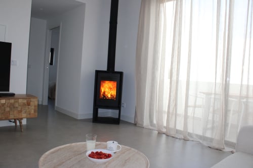 Modern living room with wood-burning stove, round table with refreshments, and sea views through large windows at Casa Mareta