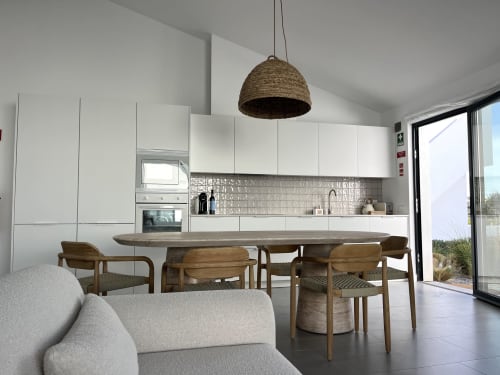 Modern villa kitchen and dining area with sea view, wooden table, contemporary white cabinetry, and woven pendant lamp in