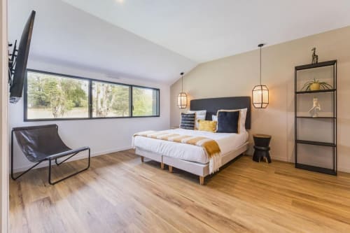 Chambre moderne à La Clairière aux Chênes avec lit queen-size, luminaires suspendus, parquet et grandes fenêtres donnant sur les arbres