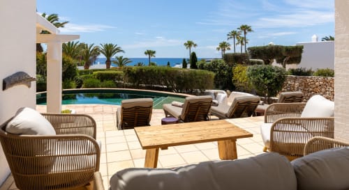 Villas Etnia Sant Lluís: Terraza con mesa de madera, sillas de ratán, piscina y vistas al mar Mediterráneo.