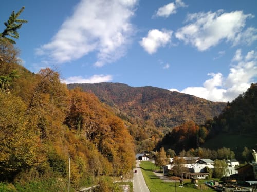 Vue de la vallée montagnarde depuis le gîte Les Boleros à Queige, avec feuillages automnaux et village alpin