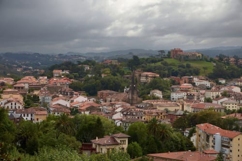 Vista aérea de Comillas, España mostrando arquitectura histórica, tejados de barro y colinas verdes bajo cielos nublados