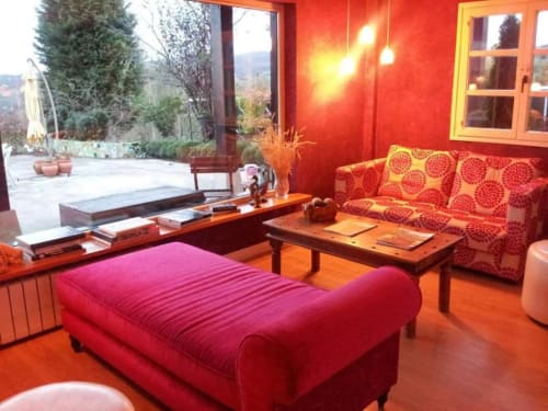 Red modern lounge at Posada Torre del Milano in Comillas with velvet seating, wooden tables, and garden views