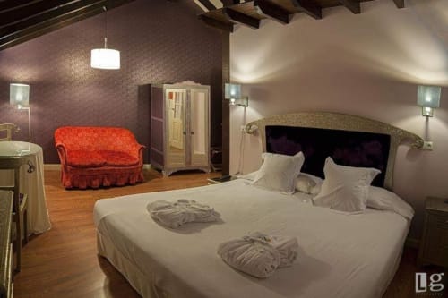Luxury bedroom at Posada Torre del Milano in Comillas with queen bed, red velvet sofa, and exposed beams