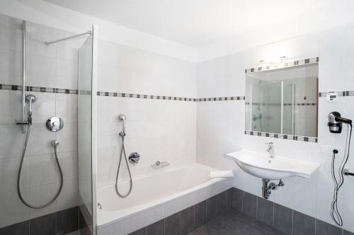 Modernes Badezimmer in der Rusctlea Apartments mit begehbarer Dusche, weißem Waschbecken, Spiegel und dunklen Fliesenakzenten