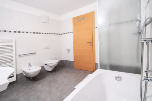Modernes Badezimmer in den Rusctlea Apartments mit Badewanne, Bidet, Toilette und orangefarbener Holztür in Selva di Valgardena
