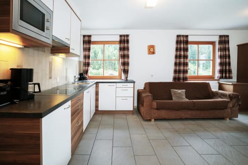 Modern two-bedroom apartment in Selva di Valgardena with open kitchen, brown sofa, and mountain views through large windows