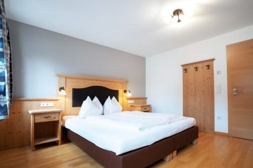 Geräumiges Schlafzimmer in den Rusctlea Apartments, Selva di Valgardena, mit Holzmöbeln, weißer Bettwäsche und Bergblick