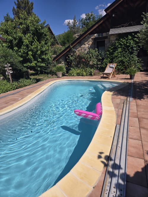 Piscine aux eaux cristallines avec flotteur rose aux Hauts d'En Castel à Ax-les-Thermes, entourée d'un jardin et d'espaces de détente
