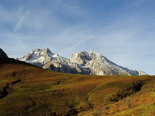 Snow-capped mountain peaks above rolling green meadows near Comillas, Spain