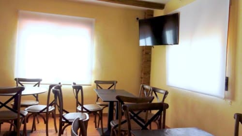 Comedor amarillo en villa Finca El Arroyo con sillas de madera, mesas, televisor pantalla plana y amplios ventanales en Alcaraz