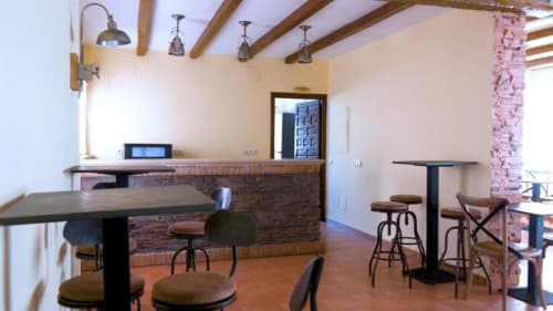 Amplia zona de bar y salón en Finca El Arroyo en Alcaraz con mostrador de ladrillo, vigas de madera y asientos de barra