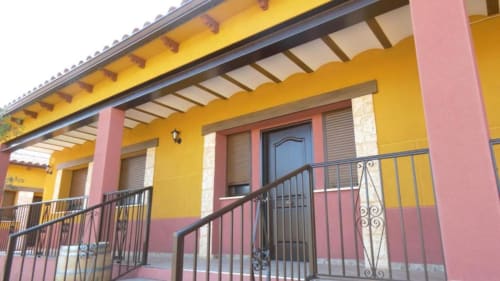Terraza colorida de villa en Finca El Arroyo, Alcaraz, con muros amarillos y rosa, barandillas metálicas y área de patio cubierto