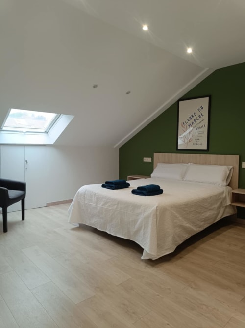 Dormitorio moderno en Santiago de Compostela con pared verde, cama de madera, tragaluz y suelo de madera.